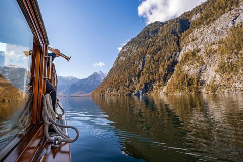 A trumpet is played on the echo wall of a tourist boat, Königssee, autumnal mountain landscape