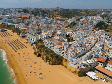 City on a hill with a lively sandy beach on the coast and numerous buildings, aerial view,