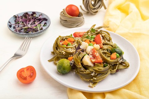 Tagliatelle green spinach pasta with tomato, pea and microgreen sprouts on a white wooden