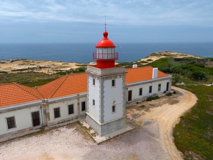 Close-up of a lighthouse and a neighbouring building overlooking the sea under a cloudy sky Aerial
