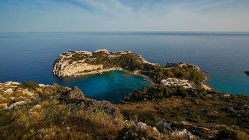 Coastal landscape with rocky cliffs and clear blue water under a sunny sky, Anthony Quinn Bay,
