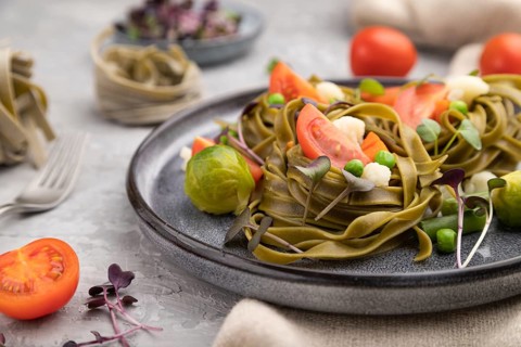 Tagliatelle green spinach pasta with tomato, pea and microgreen sprouts on a gray concrete