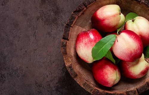 Ripe nectarine, in a wooden plate, brown background, top view, no people