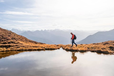 Mountaineer hiking with poles, reflected in a small mountain lake on the Krahberg, mountain