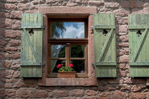 Window with green shutters and a flower pot with geraniums in a red sandstone house, Palatinate