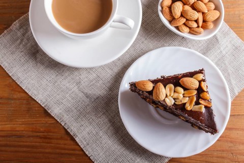 Chocolate cake with caramel, peanuts and almonds on a brown wooden background. cup of coffee, top