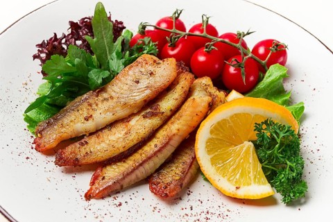 Fried Tilapia fish fillet, in spices, with cherry and salad, on a white plate, homemade, no people
