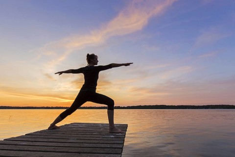 Woman practicing yoga posture Virabhadrasana II, Warrior Pose, lunging standing asana on jetty at