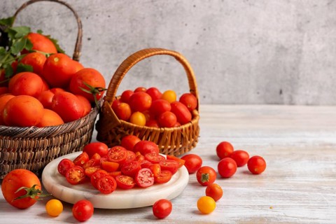 Sliced tomatoes on a white marble slab, surrounded by fresh tomatoes in baskets