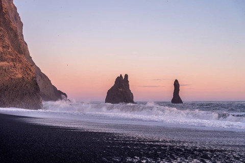 Volcanic formations on the black sand beach of Reynisfjara at sunset in Iceland