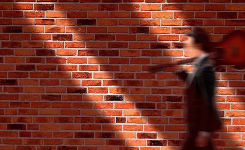 House wall with red bricks, musician carries his guitar on his shoulder, motion blur