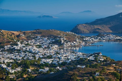 White painted houses of a coastal town, embedded in hilly landscape, surrounded by blue sea, Skala,