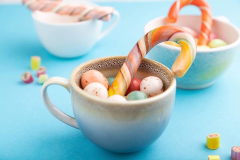Heap of multicolored caramel candies in cups on blue pastel background. close up, side view,
