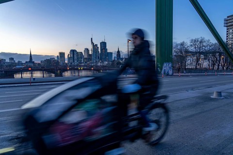 Skyline of the city centre of Frankfurt am Main, cargo bike cyclist on the rafter bridge, dusk,