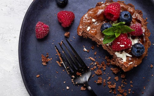 Half-eaten chocolate tartlet, on a plate, stuffed with cottage cheese and berries, breakfast,