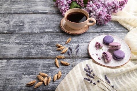 Purple macarons or macaroons cakes with cup of coffee on a gray wooden background and white linen