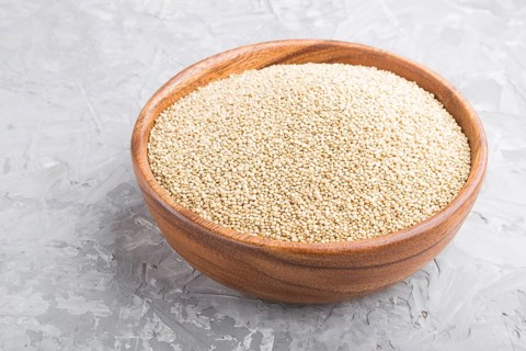 Wooden bowl with raw white quinoa seeds on a gray concrete background. Side view, close up