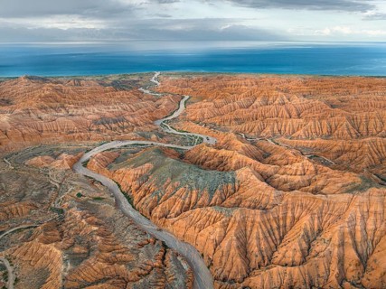 River bed runs through a landscape of eroded hills, badlands, Issyk Kul Lake in the background,