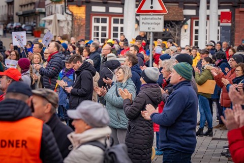 Group of people applauding at an event with security service in the foreground, Against the Right