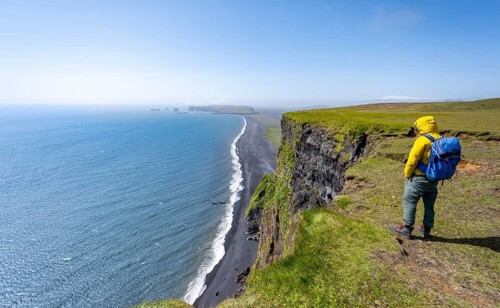 Young man standing on cliff, view from steep cliff over Reynisfjara beach, Black sand beach, Vik,