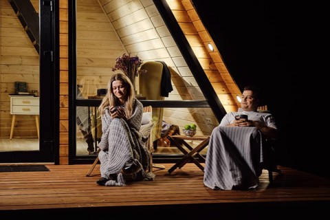 A friendly married couple is sitting on the terrace of log cabin and enjoys warm evening
