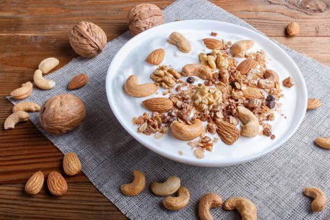 White plate with greek yogurt granola, almond, cashew, walnuts on brown wooden background. close up