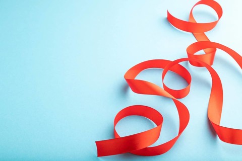 Red coral ribbon on a blue pastel background. Celebration concept. Side view, copy space