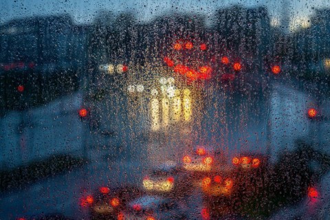 Rainy weather, road traffic, raindrops on a window pane, behind, blurred, lights of vehicles on a
