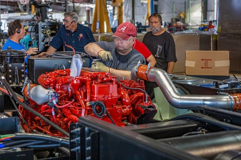 Worker installing a Cumins ISL diesel engine on chassis at Tiffin Motorhomes factory in Red Bay,