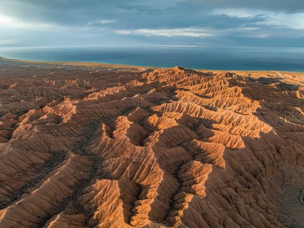 Landscape of eroded hills, badlands at sunset, Issyk Kul Lake in the background, aerial view,