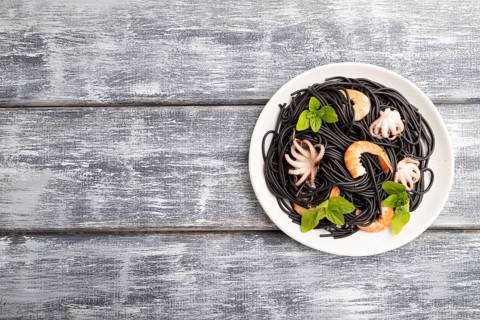 Black cuttlefish ink pasta with shrimps or prawns and small octopuses on gray wooden background.