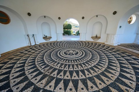 A detailed mosaic on the floor of a white circular building with open arches to the outside,