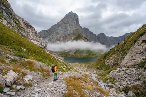 Mountaineer on a hiking trail with a view of rocky, cloud-covered mountains and Wolayersee, hiking