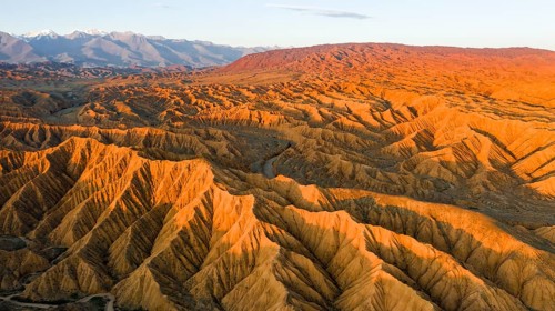 River bed runs through a landscape of eroded hills, badlands at sunset, mountain peaks of the Tian
