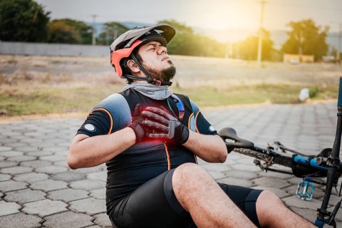 Cyclist on the pavement with chest pain. Concept of cyclist suffering with hand on his chest. Male