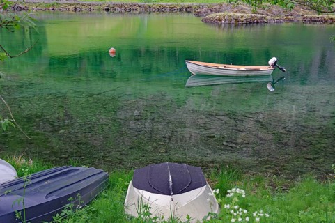 A small boat floats on a calm green lake, surrounded by grass and nature, Mindresundet, Stryn,