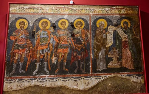 Medieval fresco depicting saints and apostles, all with glowing halos and textual writings on