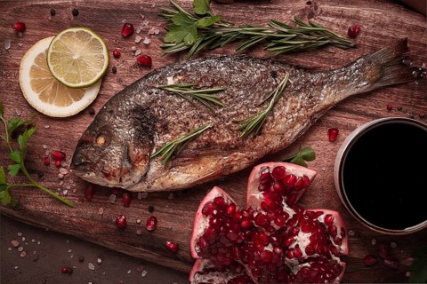 Fried dorado fish, with spices and herbs, on a wooden board, pomegranate sauce, close-up, no people