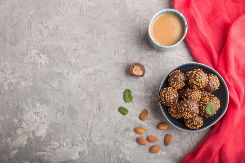 Chocolate caramel ball candies with almonds and a cup of coffee on a gray concrete background and