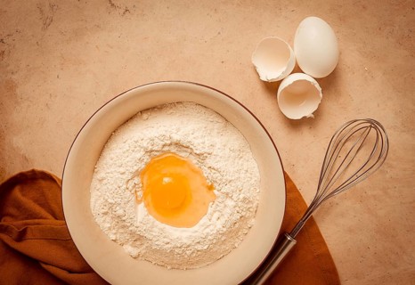 Food background, concept, plate with wheat flour, broken egg, whisk, kitchen towel, on a beige