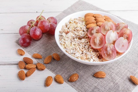A plate with muesli, almonds, pink grapes on a white wooden background. close up