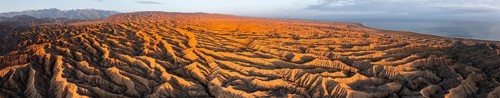 Panorama, landscape of eroded hills, badlands at sunset, Lake Issyk Kul in the background, aerial