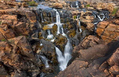 Waterfalls between orange-coloured rocks on the Treur River, Bourke's Luck Potholes, long exposure,