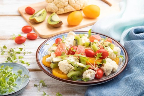 Vegetarian salad of cauliflower cabbage, kiwi, tomatoes, microgreen sprouts on white wooden