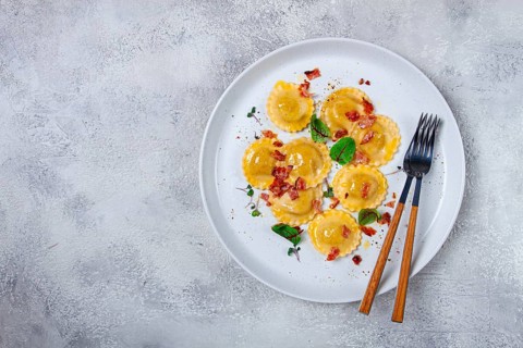 Fresh ravioli, with butter, spices and herbs, fried bacon, on the table, top view, light