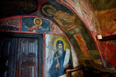 Scene of an orthodox church with religious wall paintings and a wooden door in the background,