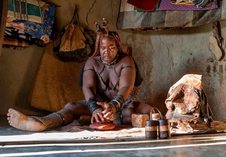 Traditional Himba woman making ochre body paint from fat and ochre, interior of the first woman's