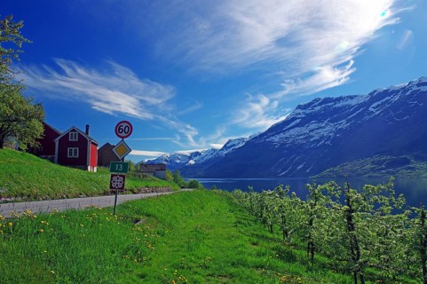 Country road leads along a church and green meadows, surrounded by mountains and a fjord, spring,