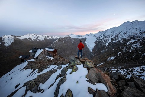 Hiker looking at mountain panorama and glacier, mountain hut Ramolhaus in autumn with snow, at