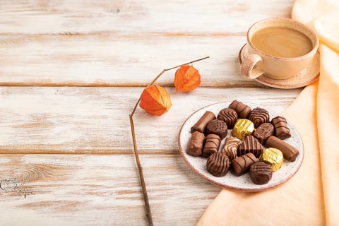 Chocolate candies with cup of coffee and physalis flowers on a white wooden background and orange